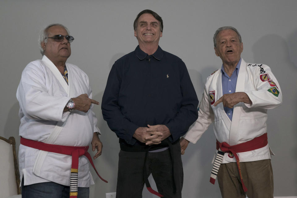 Brazilian presidential candidate Jair Bolsonaro smiles after receiving a honorary black belt from Jiu-Jitsu masters Robson Gracie, right, and Joao Carlos Austregesilo Athayde, in Rio de Janeiro, Brazil, Thursday, Oct. 25, 2018. Bolsonaro was awarded the honorary black belt out a respect for surviving a recent knife attack where he was wounded in the abdomen by a crazed attacker. (AP Photo/Leo Correa)