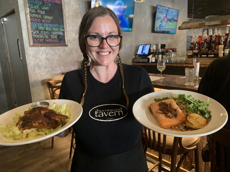 Adrienne Sanders, a waitress at the new Burntwood Tavern restaurant at The Trails Shopping Center in Ormond Beach, holds plates of cedar planked salmon and blackened grouper on Thursday, Aug. 26, 2021.