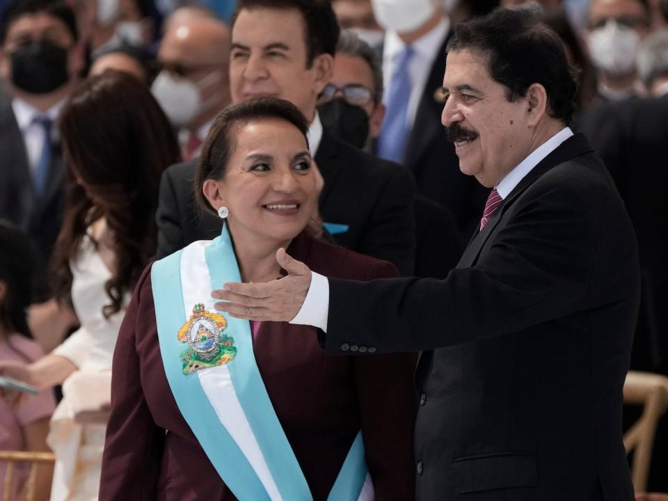 President Xiomara Castro smiles after receiving the presidential sash, as her husband former President Manuel Zelaya who was ousted by a military coup in 2009, right, applauds during her inauguration as the first female president, in Tegucigalpa, Honduras, Thursday, Jan. 27, 2022.