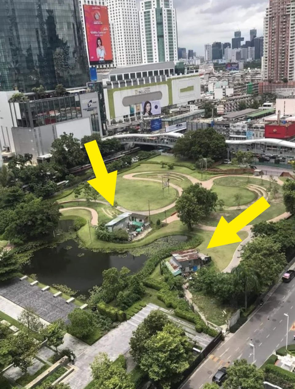 Aerial view of a city park with winding paths, a pond, and surrounded by high-rise buildings