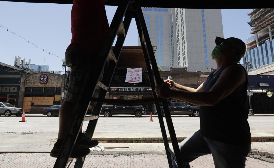 A sign directed at Texas Gov. Greg Abbott is seen behind workers preparing another pub that they hope to reopen soon in Austin, Texas, Monday, May 18, 2020. Texas continues to go through phases as the state reopens after closing many non-essential businesses to help battle the spread of COVID-19. (AP Photo/Eric Gay)