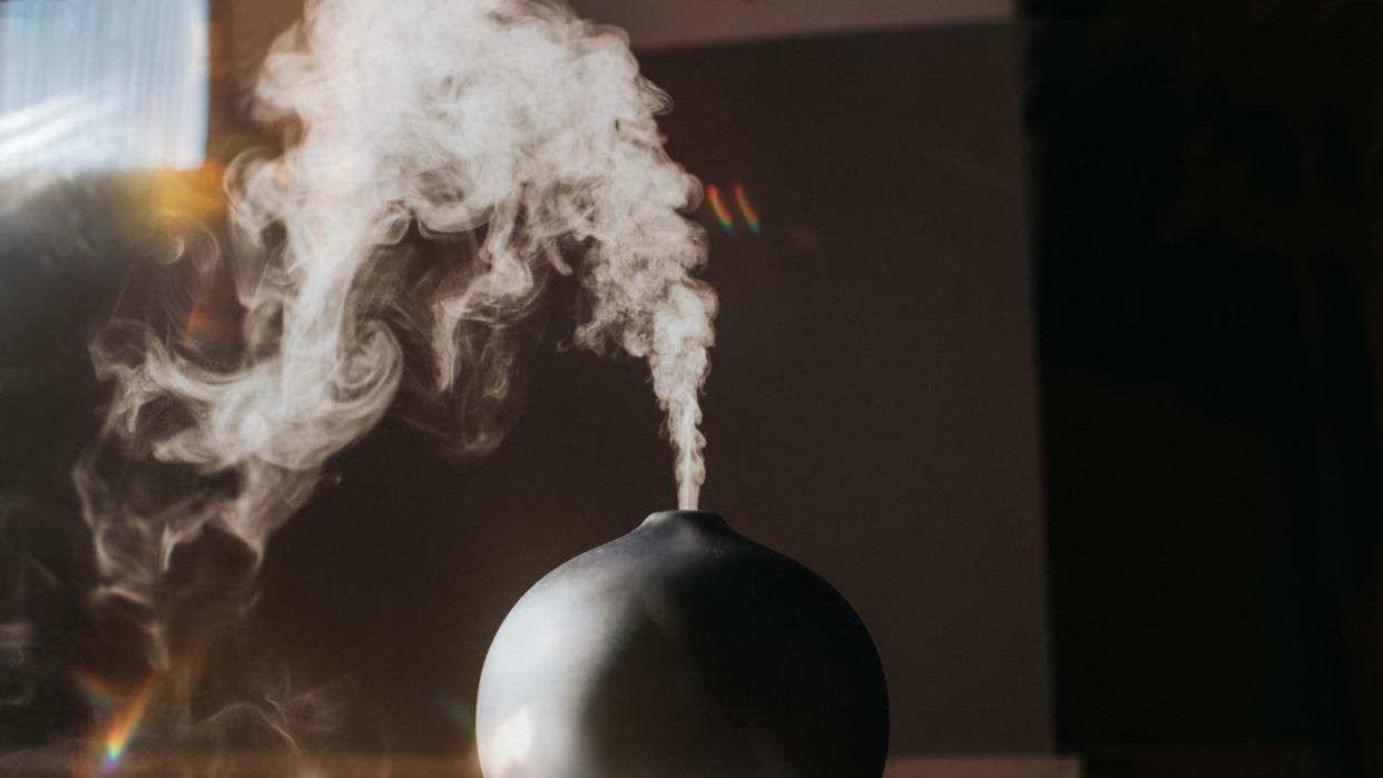  A black humidifier turned on with a puff of white vapor above it  