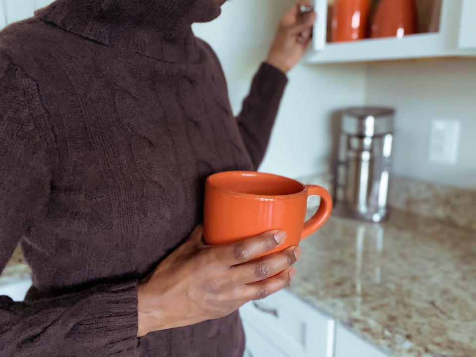 Woman taking out mug from cupboard. (Getty Images)