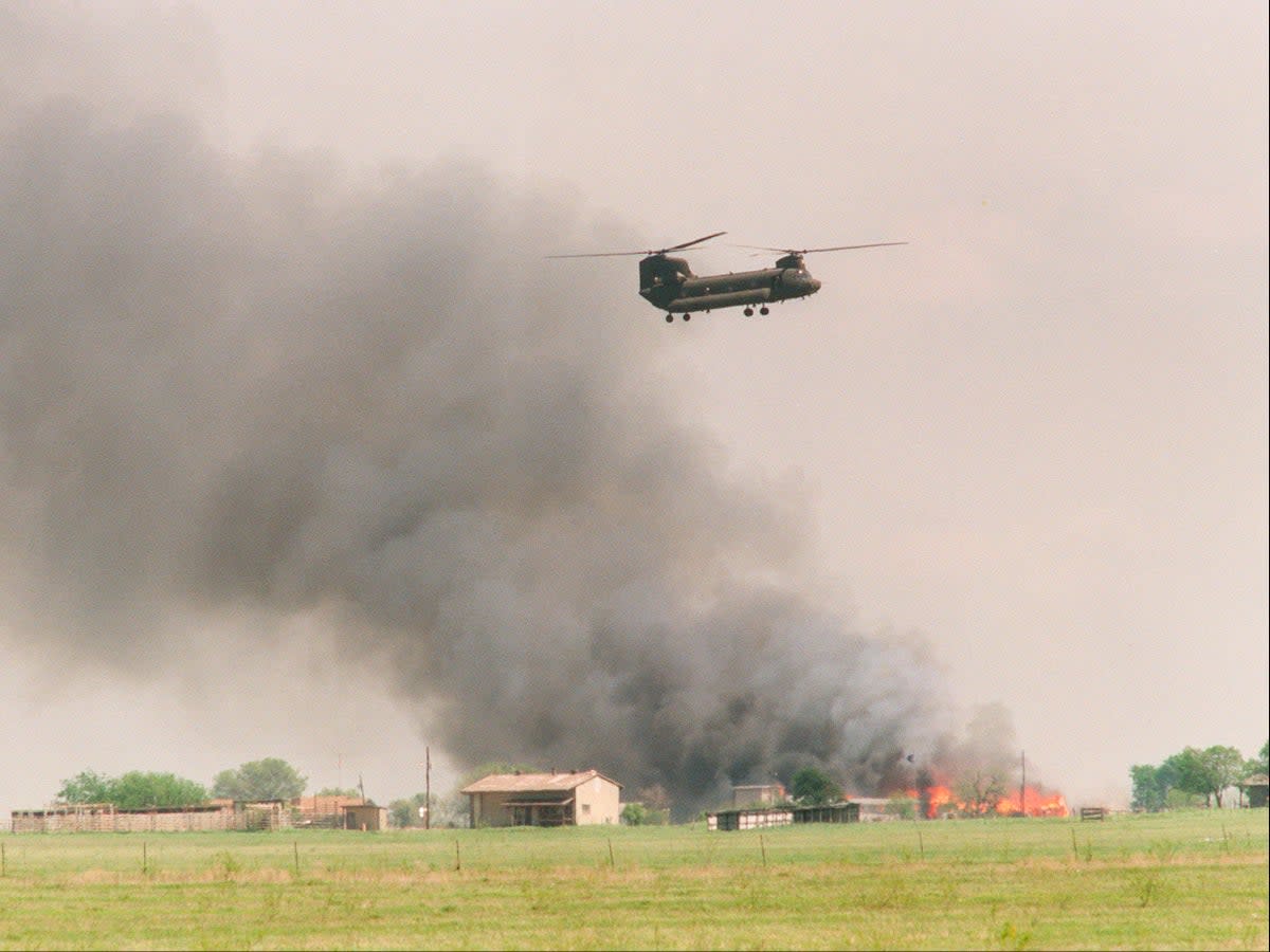 A National Guard helicopter flies past the burning Branch Davidian cult compound in Waco, Texas on 19 April 1993 (TIM ROBERTS/AFP via Getty Images)