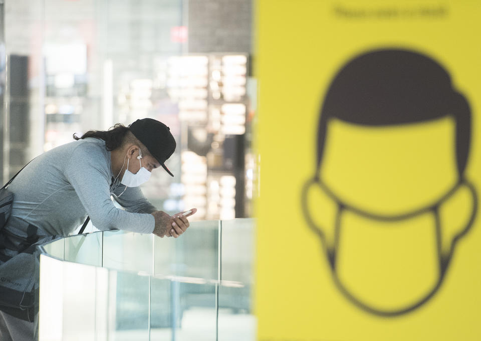 A man wears a face mask as he browses on his phone in a shopping mall in Montreal, Sunday, August 2, 2020, as the COVID-19 pandemic continues in Canada and around the world. The Quebec government has made the wearing of masks and face coverings mandatory in all public spaces as of July 18 and will increase the number of people allowed to gather indoors and outdoors to 250 people as of August 3. THE CANADIAN PRESS/Graham Hughes