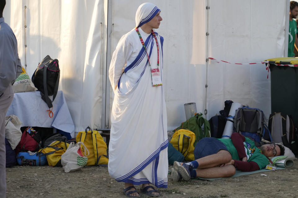 A Sister of Charity stands by a pilgrim sleeping at Parque Tejo in Lisbon where Pope Francis will preside over a mass celebrating the 37th World Youth Day, Sunday, Aug. 6, 2023. An estimated 1.5 million young people filled the parque on Saturday for Pope Francis' World Youth Day vigil, braving scorching heat to secure a spot for the evening prayer and to camp out overnight for his final farewell Mass on Sunday morning. (AP Photo/Gregorio Borgia)