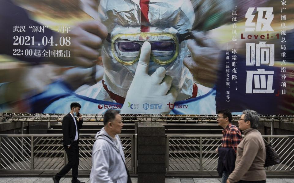 Pedestrian walk past a billboard promoting a television show on China's fight against Covid-19 in Shanghai - Bloomberg