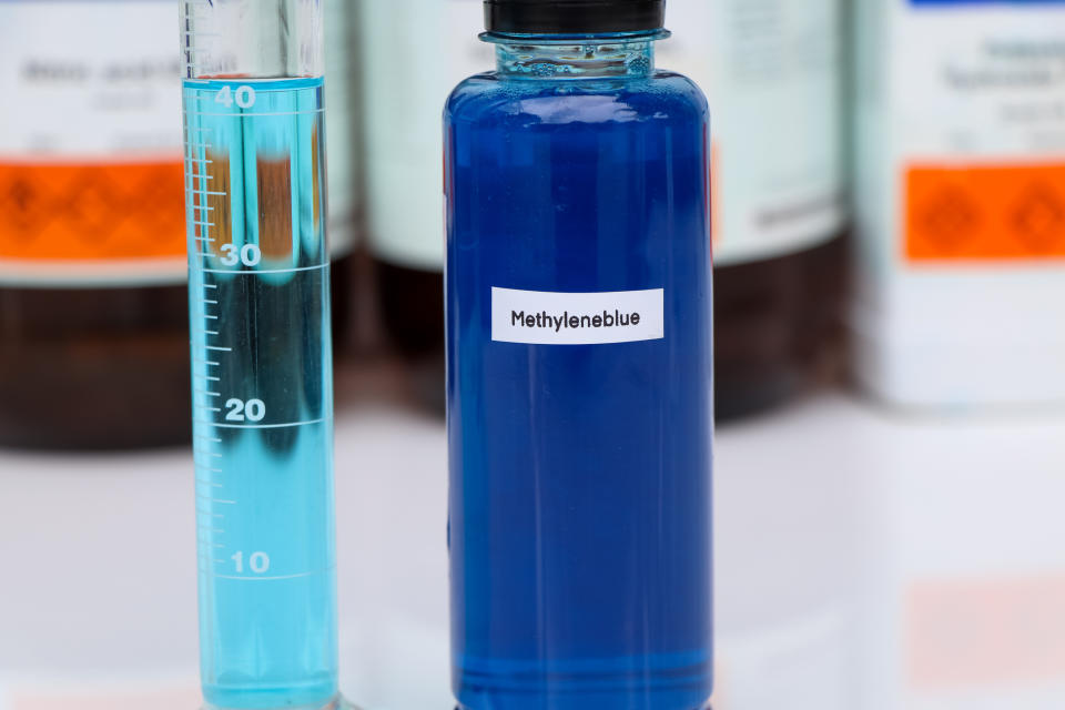 A vial labeled "Methylene Blue" stands next to a graduated cylinder with liquid inside. Other containers are in the background