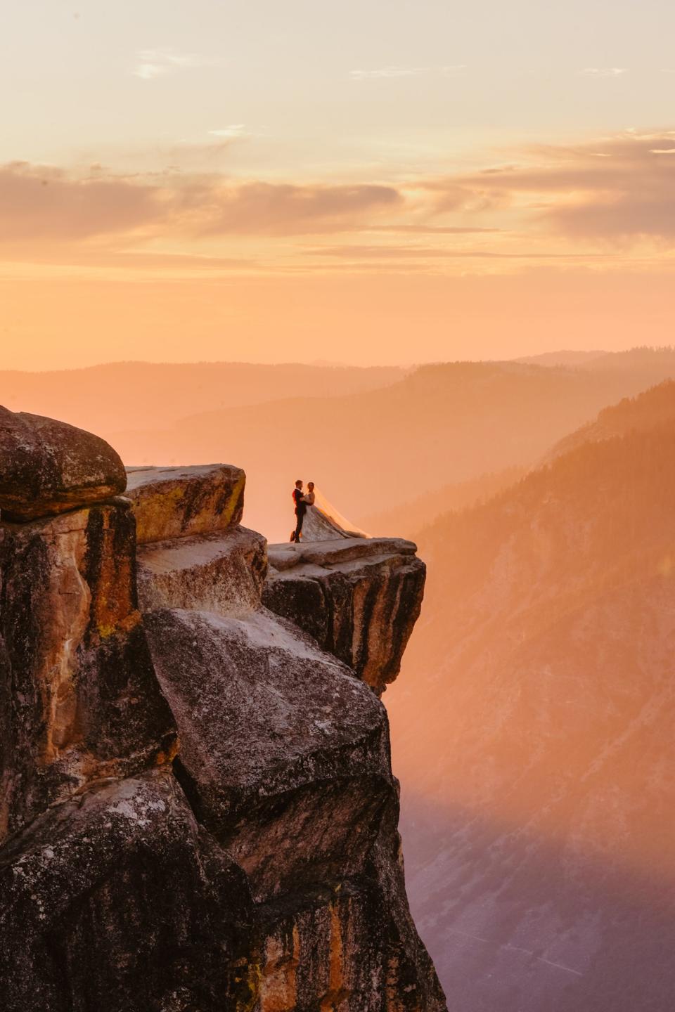 A bride and groom embrace on a cliff.