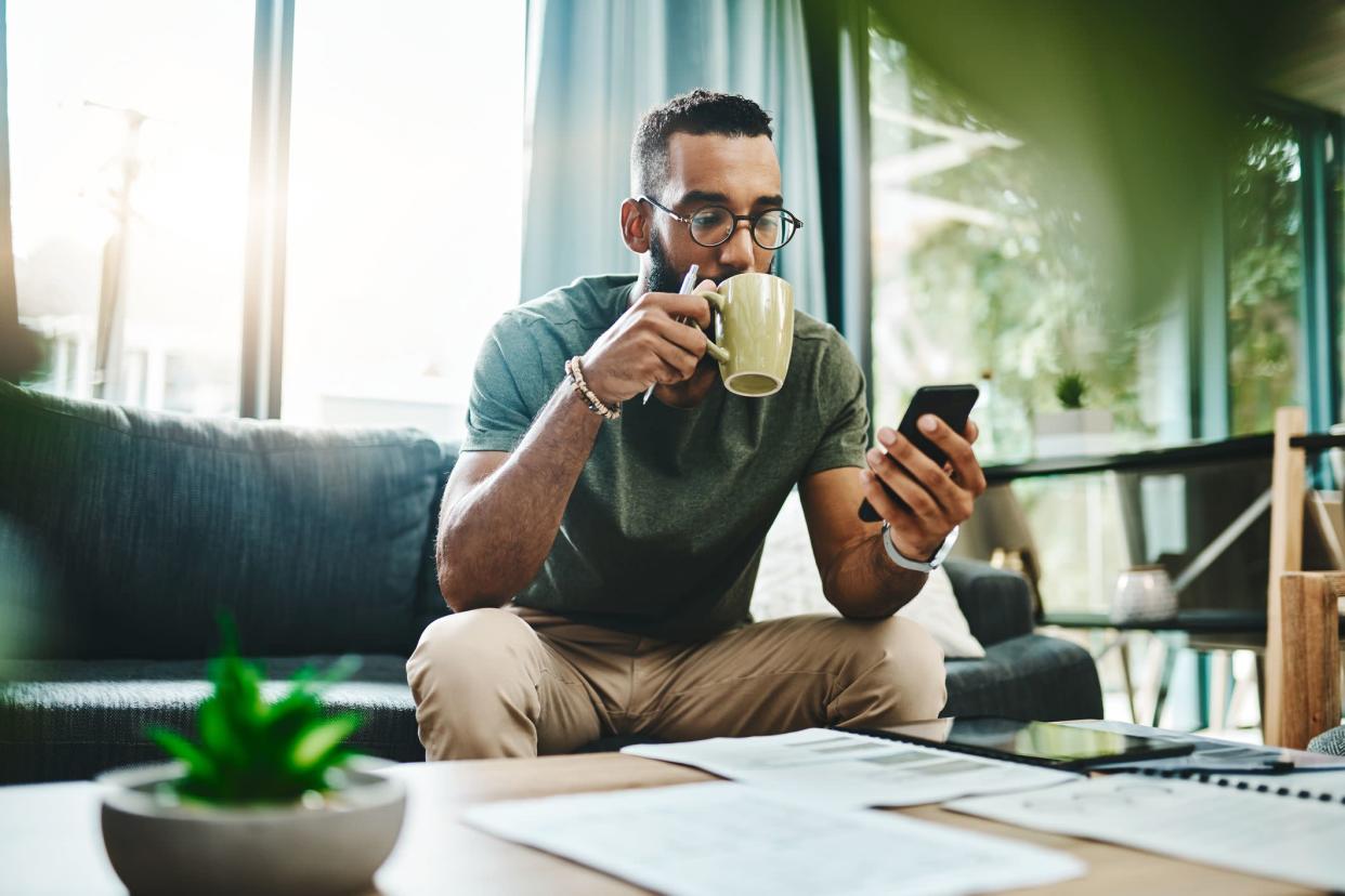 Shot of a young man using a smartphone while going over his finances at home