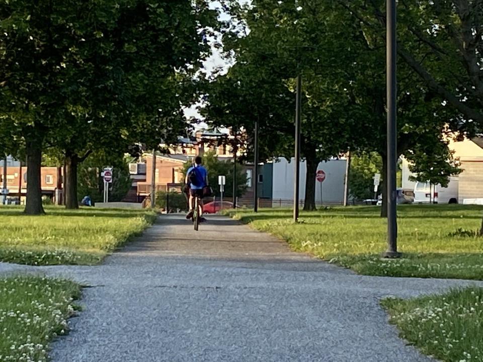 Teens on bikes pedal through Penn Park, fishing poles in tow.