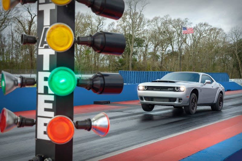 A Dodge Challenger hellcat popping a wheelie while launching at a drag strip