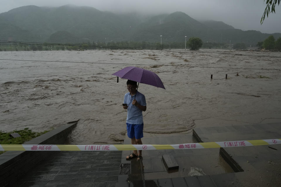 A resident stands near a swollen river in the mountainous outskirts of Beijing, Tuesday, Aug. 1, 2023. Chinese state media report some have died and others are missing amid flooding in the mountains surrounding the capital Beijing. (AP Photo/Ng Han Guan)