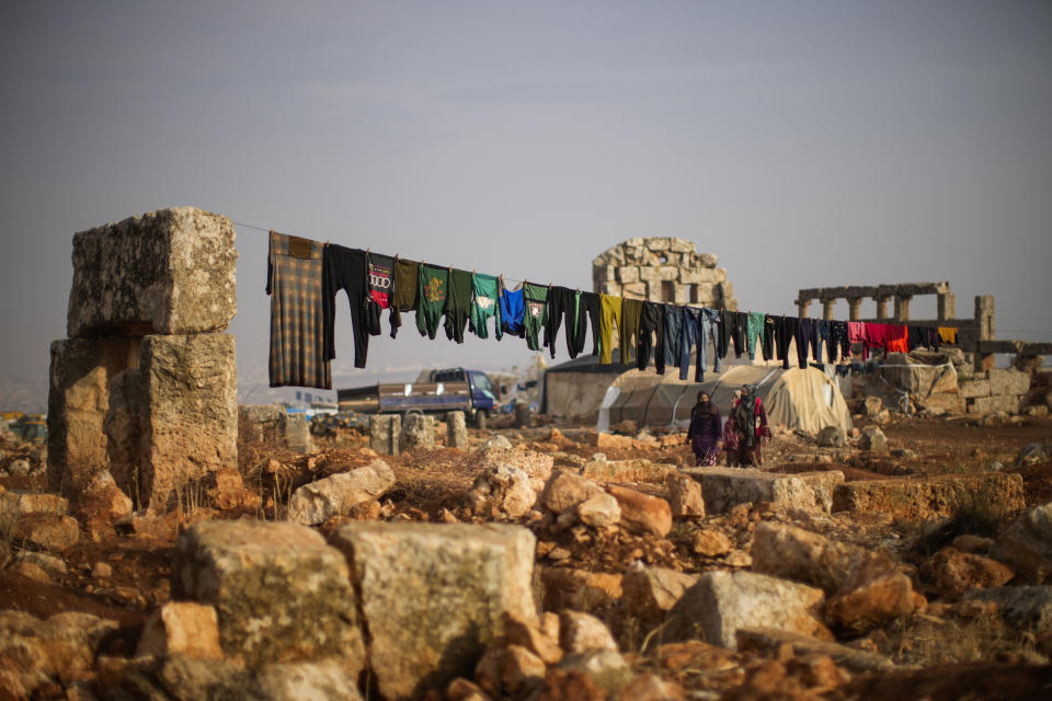 FILE - Syrian displaced people walk next to ancient Roman era ruins where they have set their tends in Sarmada district, north of Idlib city, Syria, Thursday, Nov. 25, 2021. Fallout from the 2-month-old war in Ukraine is worsening long-term humanitarian crises elsewhere, including in Syria. (AP Photo/Francisco Seco, File)