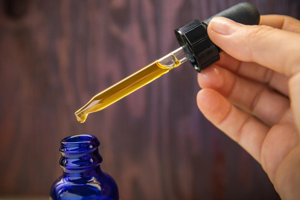 A dose of CBD (Cannabidiol) oil measured out of blue bottle with dropper on wooden background