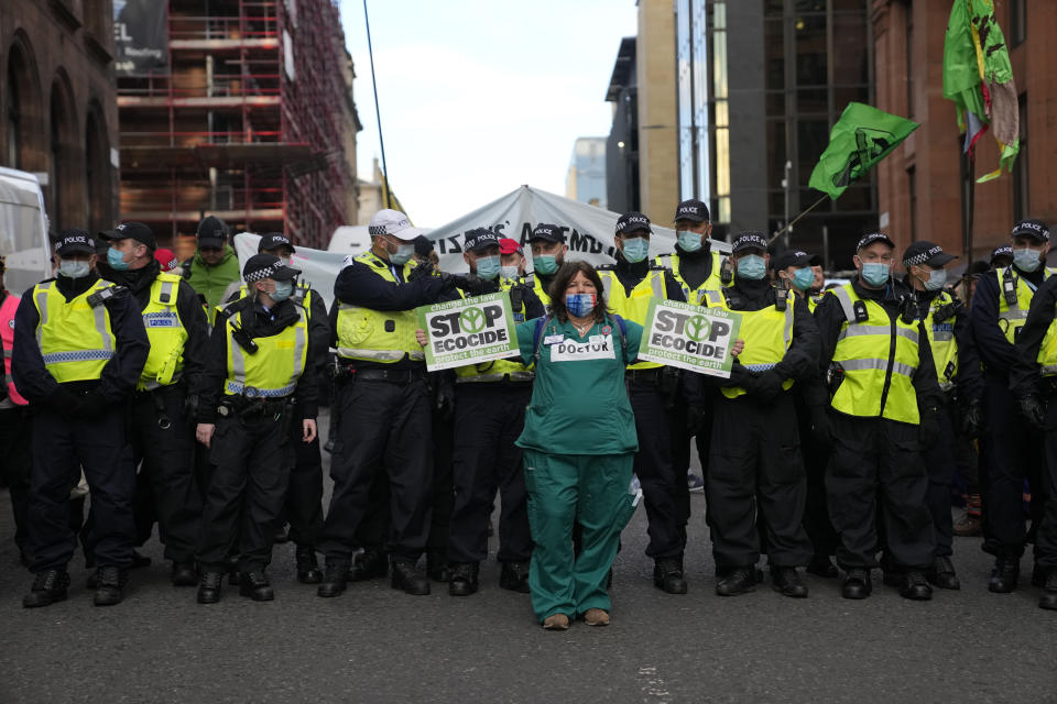 A climate protester from Doctors for Extinction Rebellion stands in front of a line of police officers during a demonstration against 'Greenwashing' (an attempt to make people believe that your company or government is doing more to protect the environment than it really is) near the COP26 U.N. Climate Summit in Glasgow, Scotland, Wednesday, Nov. 3, 2021. (AP Photo/Alastair Grant)