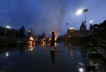 A boy wades through the water next to the burning pyres of people, who died in Saturday's earthquake, during the cremation along a river in Kathmandu, Nepal April 28, 2015. REUTERS/Adnan Abidi