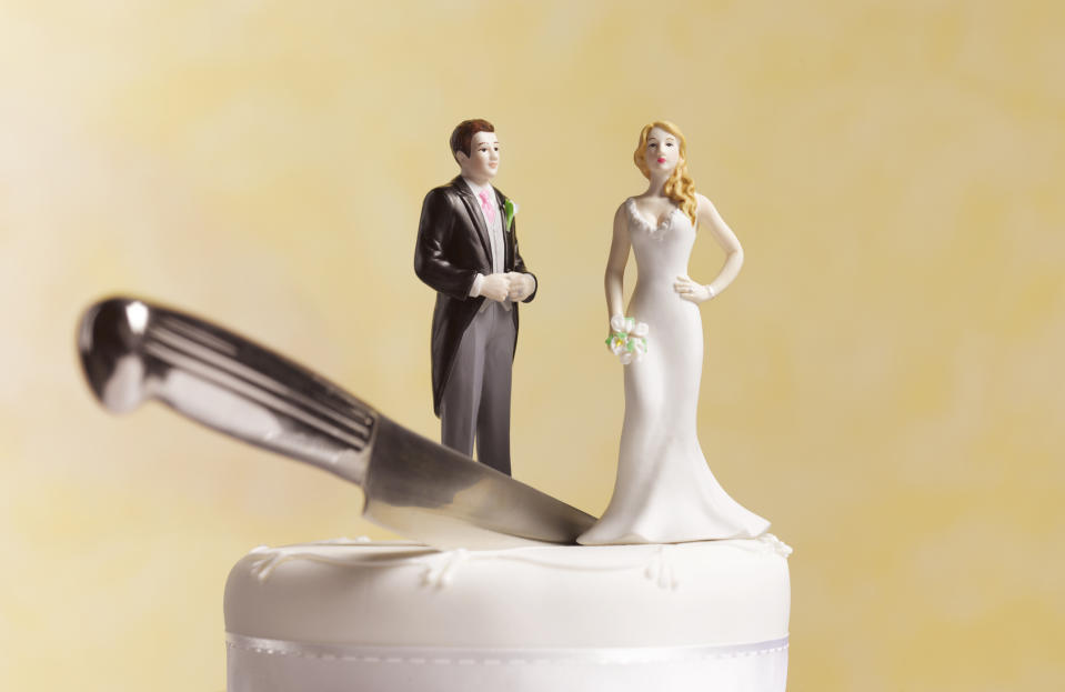 A bride and groom figurine adorn a wedding cake, with a knife placed nearby. The bride is in a sleek white gown, and the groom wears a black suit with a white shirt