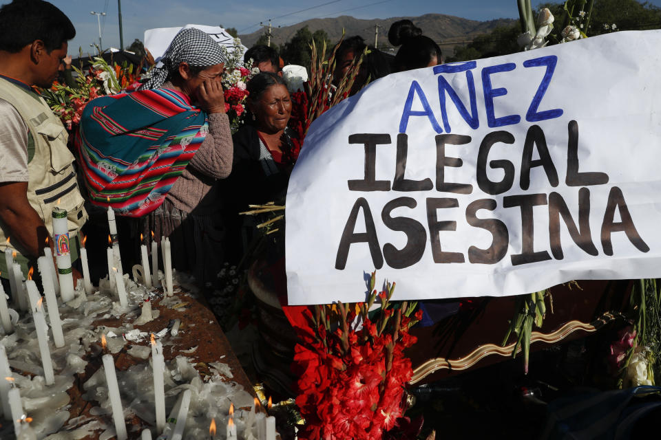 People attend the funeral of supporters of former President Evo Morales killed during clashes next to a banner reading in Spanish "Anez illegal killer" referring to Bolivia's interim President Jeanine Anez in Sacaba, Bolivia, Saturday, Nov. 16, 2019. Bolivian security forces clashed with Morales' supporters in a central town Friday, leaving at least five people dead, dozens more injured and escalating the challenge to the country's interim government to restore stability. (AP Photo/Juan Karita)