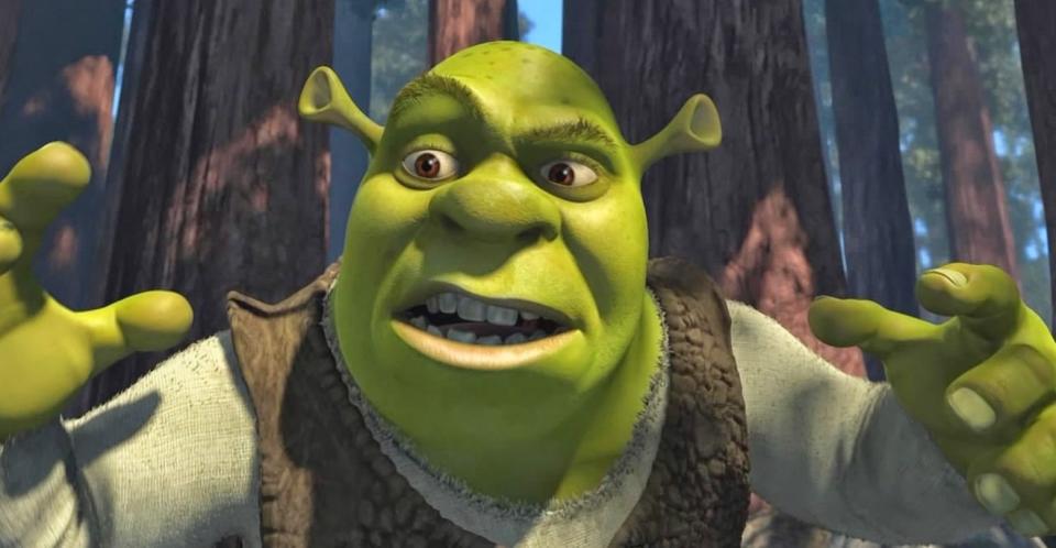 Shrek stands in the woods and gestures while talking