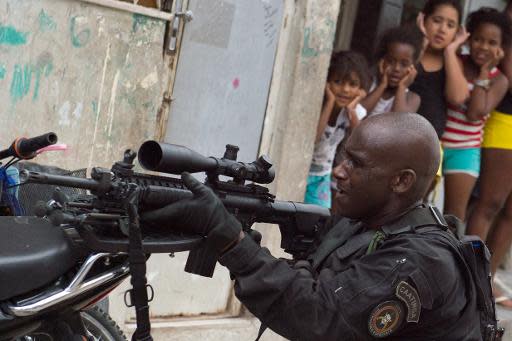 Unas niñas se tapan los oídos mientras un policiía de la unidad especial paramilitar, BOPE, avanza por las calles de la 'Favela da Mare', al norte de Río de Janeiro, el 26 de marzo de 2014 (AFP | Christophe Simon)