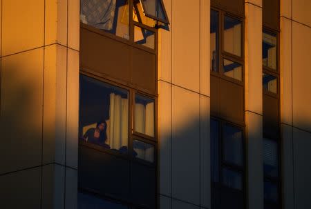 A woman looks out of a window in the Burnham Tower residential block, as residents were evacuated as a precautionary measure following concerns over the type of cladding used on the outside of the building on the Chalcots Estate in north London, Britain, June 24, 2017. REUTERS/Hannah McKay