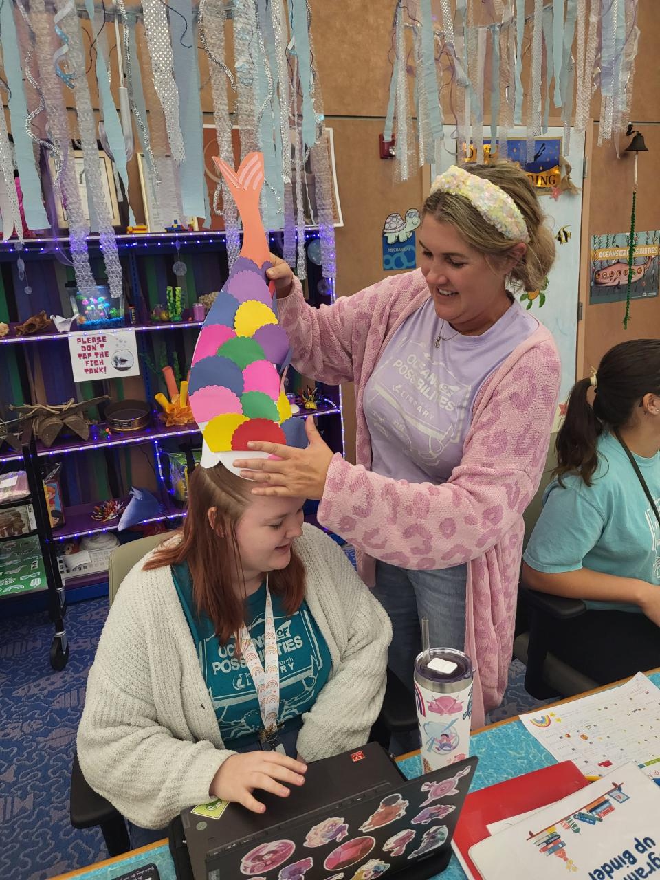 Librarians Brooke Jones, 20 and Megan Hutchinson, 38, show off the fish crown Tuesday. The crown will go to Emily Daigle, the librarian who suggested the name Bubbles for the beta fish that serves as the summer reading program's mascot.