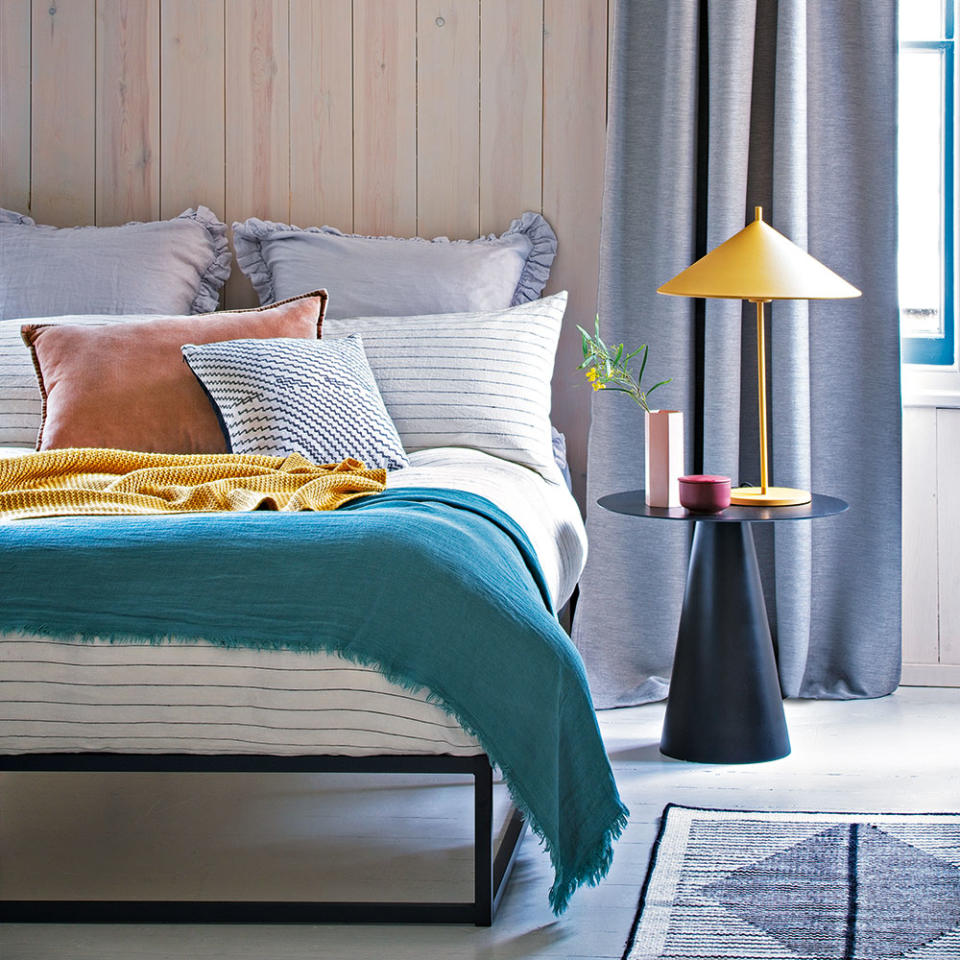 bedroom with wooden wall bed with designed cushion lamp on bedside table and grey curtain