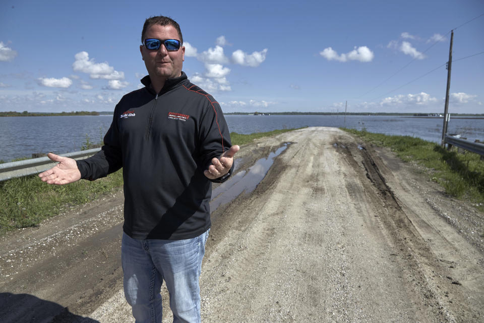 In this May 10, 2019 photo, Brett Adams gestures as he stands where the road to his flooded farm disappears under flood waters, with the farm buildings seen in the background, in Peru, Neb. Adams had thousands of acres under water, about 80 percent of his land, this year. The water split open his grain bins and submerged his parents' house and other buildings when the levee protecting the farm broke. (AP Photo/Nati Harnik)
