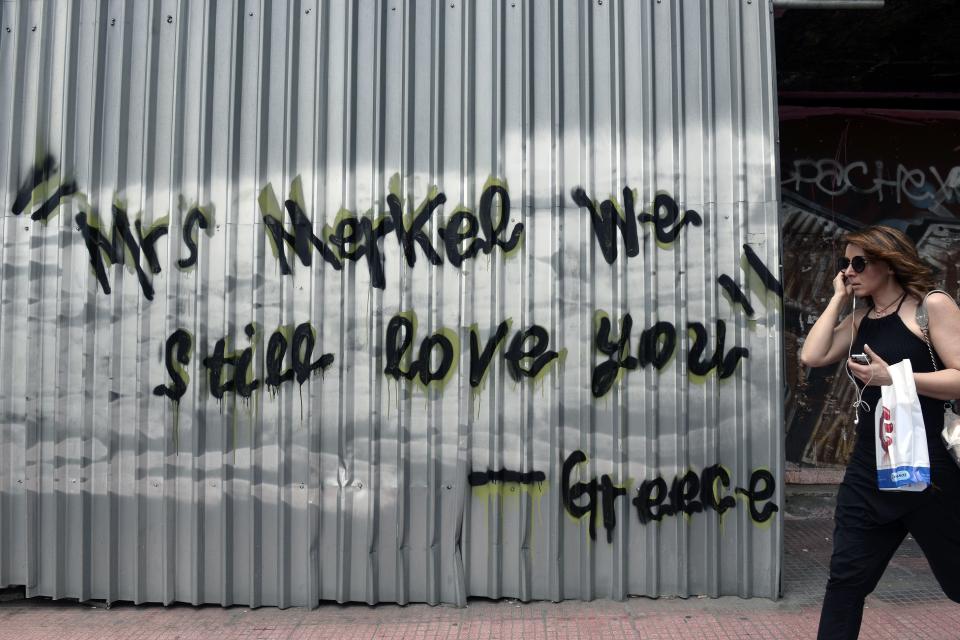 A woman walks past a slogan reading 'Mrs Merkel -we still love you-Greece' on a sheet metal covering a burned down building in Athens on June 10, 2015. (LOUISA GOULIAMAKI/AFP/Getty Images)