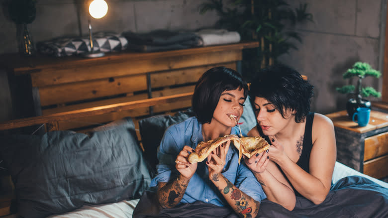 two women eating pizza in bed