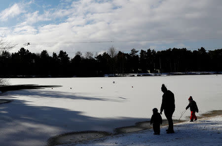 People walk around the side of a frozen lake in Elveden Forest, Suffolk, Britain, February 27, 2018. REUTERS/Paul Childs