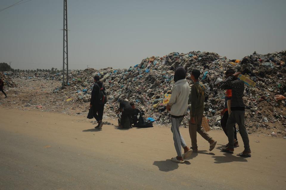 People walk past a garbage dump in Khan Younis, in the southern Gaza Strip, on May 22, 2024.