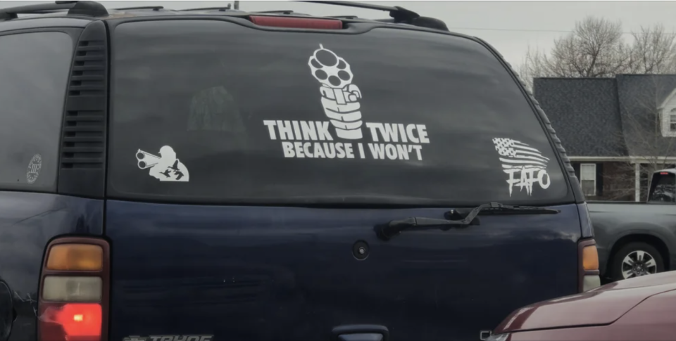 Rear window of a vehicle with decals of a gun and the text "THINK TWICE BECAUSE I WON'T"