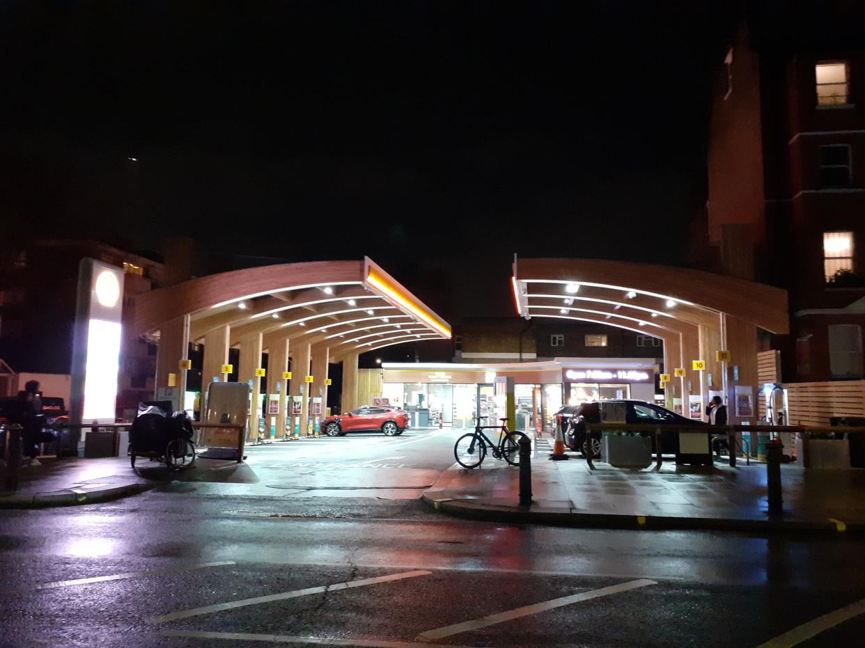 Shell Recharge in Fulham, at night. It has bright lights and wooden canopies in place of the metal canopies at traditional gas stations.