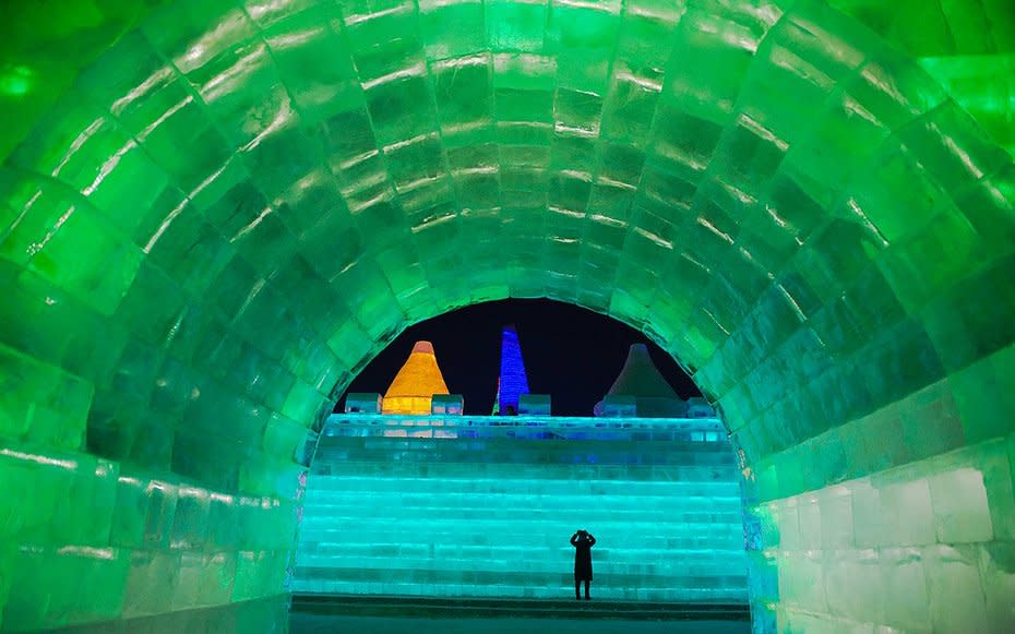 <p>A woman takes a photo as she visits an iglooilluminated by green huedlights at the festival.</p>