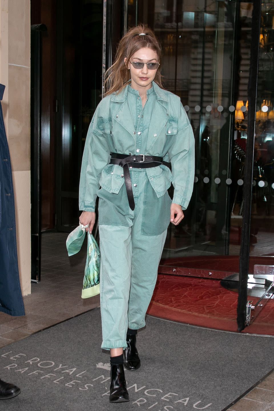 <p>In an oversized green jumpsuit, black ankle boots, black waist-cinching belt, and sunglasses. </p>