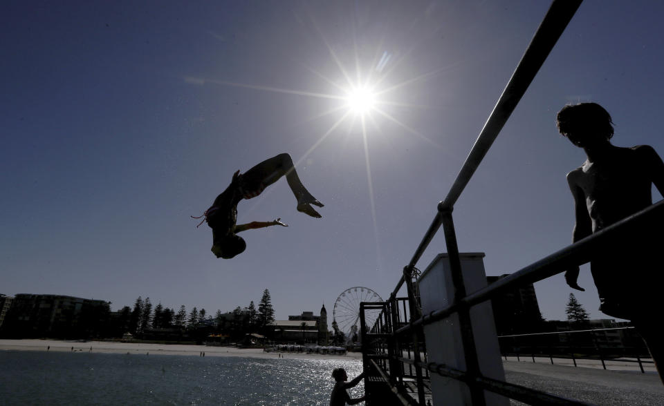 In this Jan. 24, 2019, photo, a beachgoer jumps off a jetty at Glenelg Beach in Adelaide, Australia, as temperatures climb to 45 Celsius (113 ‎Fahrenheit). Australia has sweltered through its hottest month on record in January and the summer of extremes continues with wildfires razing the drought-parched south while expanses of the tropical north are flooded. (Kelly Barnes/AAP Image via AP)