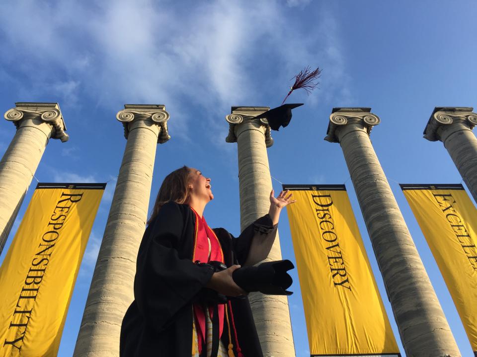 Vrouw gooit haar pet in de lucht om haar afstuderen aan de Universiteit van Missouri te vieren.