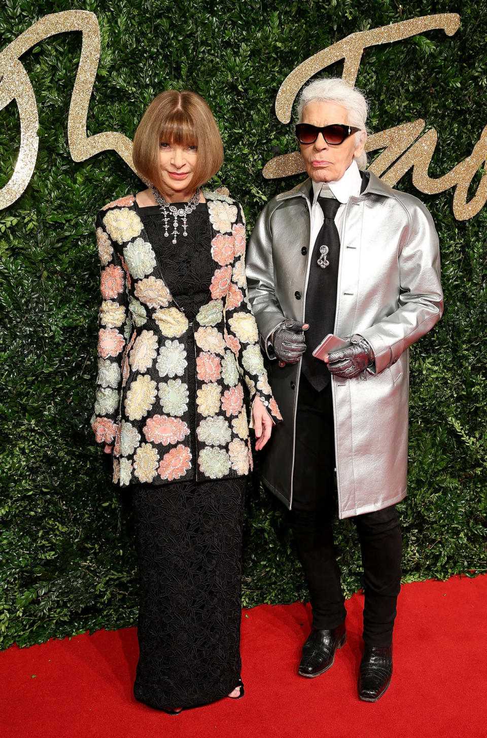 Anna Wintour in a black lace dress and floral jacket, and Karl Lagerfeld in a silver jacket and matching gloves. 