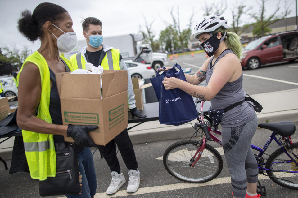 In this Thursday, May 28, 2020, photo, volunteers hand groceries to Tina Grace during a food distribution drive sponsored by Island Harvest Food Bank in Valley Stream, N.Y. The Valley Stream stream donations were just one of many events Island Harvest has conducted throughout the area recently. (AP Photo/Mary Altaffer)