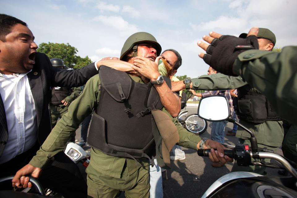 Opponents to Venezuela's President Nicolas Maduro, behind and left, scuffle with a Bolivarian National Guard officer who is loyal to President Nicolas Maduro during clashes with rebel soldiers and anti-government protesters outside La Carlota military airbase in Caracas, Venezuela, Tuesday, April 30, 2019. Venezuelan opposition leader Juan GuaidÃ³ and jailed opposition leader Leopoldo Lopez took to the streets with a small contingent of heavily armed troops early Tuesday in a bold and risky call for the military to rise up and oust Maduro. (AP Photo/Boris Vergara)