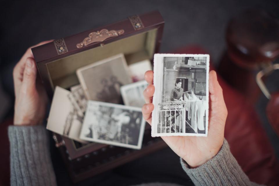 hands of woman discovering a treasure chest full of photographs and holding an old black and white photograph of a smiling woman standing on a balcony in rome in 1960s