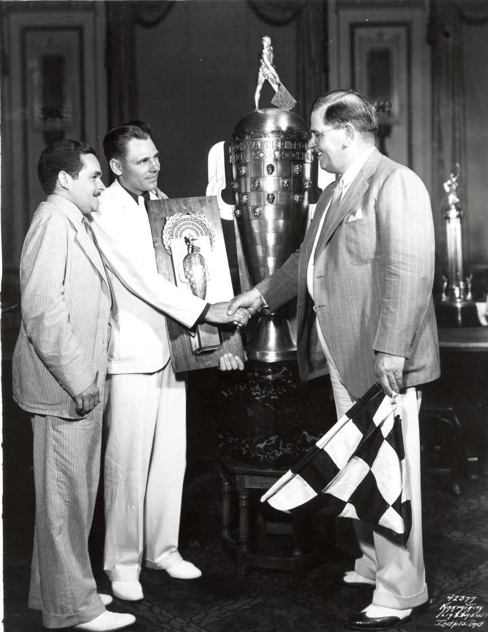 Louis Meyer. center, receives the Borg-Warner trophy after winning the Indianapolis 500 in 1936. He'd already  finished the milk at this point.