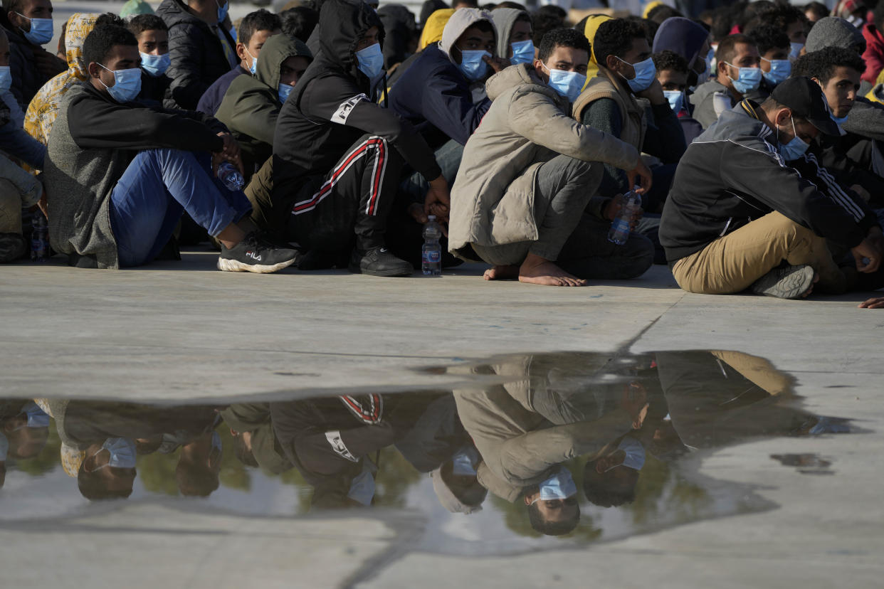 Cluods are reflected in a puddle as migrants and refugees sit on the pier after they disembarked in the port of Roccella Jonica, Calabria region, southern Italy, Sunday, Nov. 14, 2021. The Italian Coast Guard rescued Sunday morning off the cost Calabria over 250 young men and boys, mostly from Egypt. (AP Photo/Alessandra Tarantino)