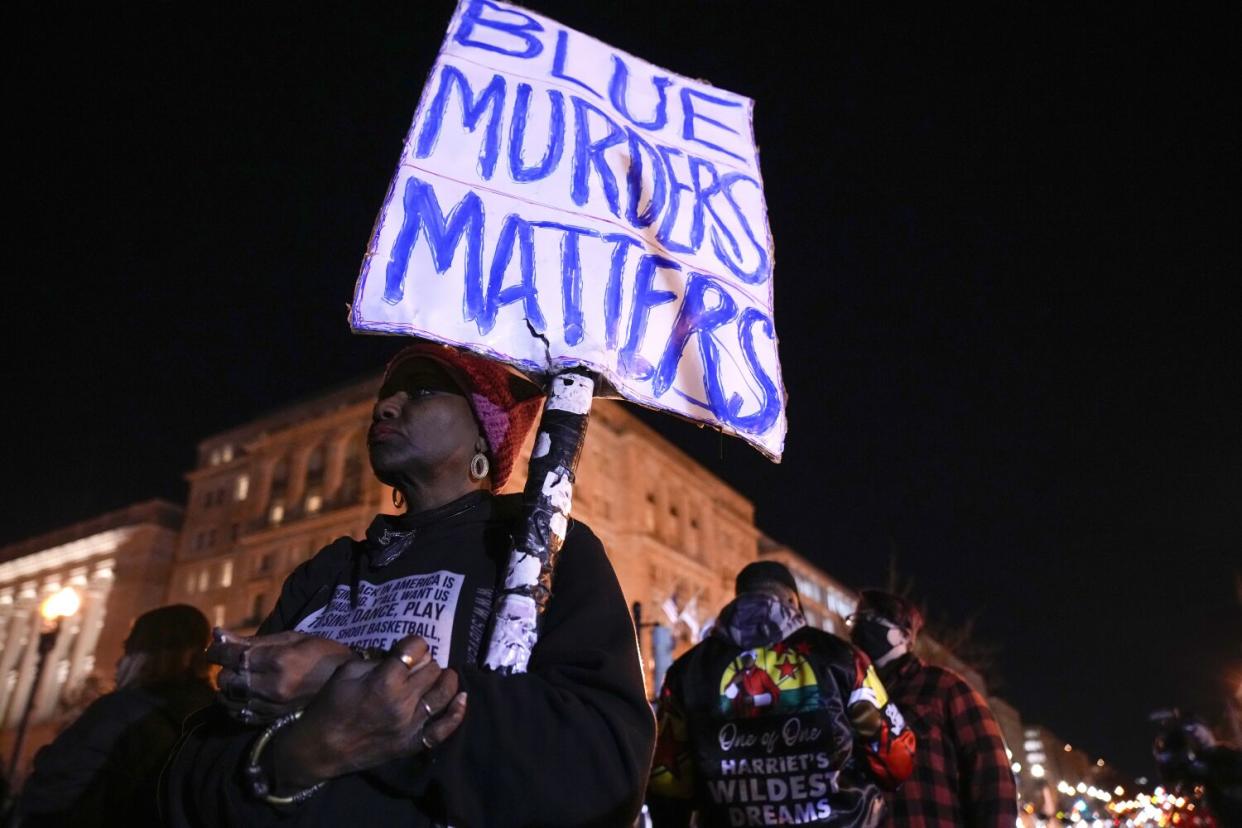 A woman holding a sign reading "Blue murders matters" at a protest in the dark