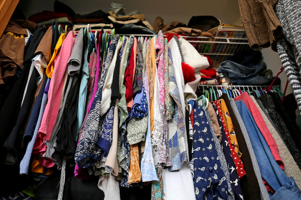 A messy young women's closet is fill with many outfits of colorful clothing, shirts, and dresses.