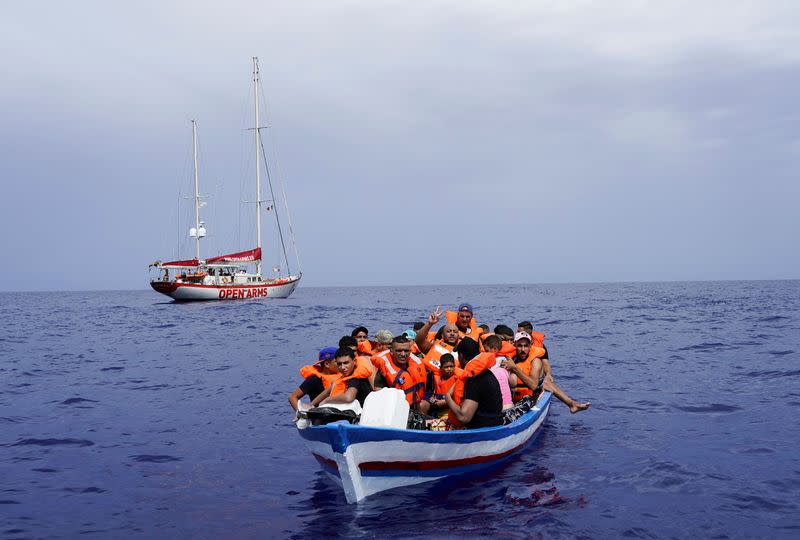 Migrantes esperan en una embarcación de madera a ser rescadatos por la Guardia Costiera italiana en el Mediterráneo