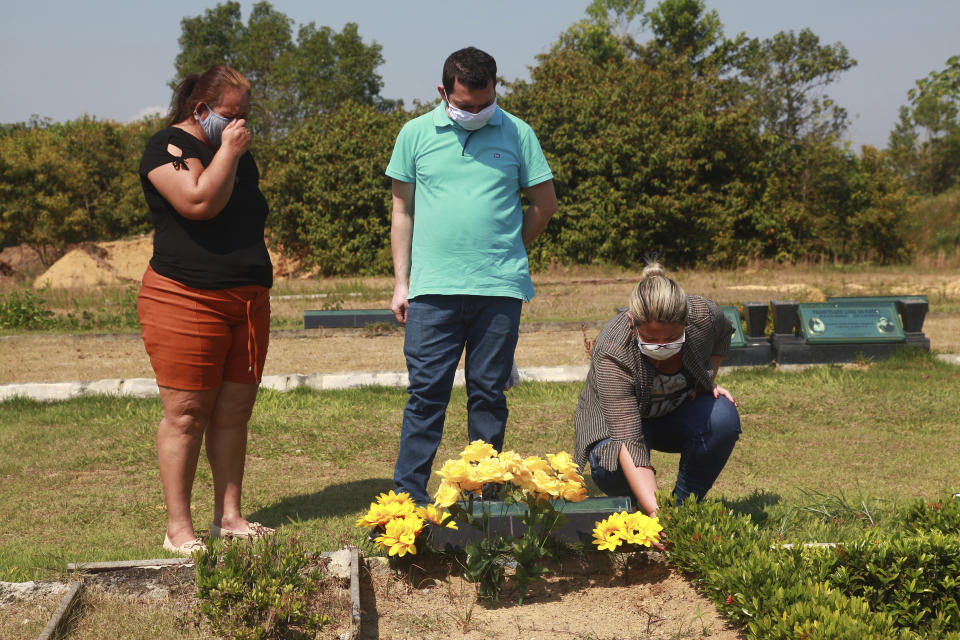 Sisters Valeria Melo da Silva, left, and Viviane, her husband Luigi do Nascimento visit the grave of their mother who died of COVID-19, at a cemetery in Manaus, Brazil, Tuesday, Aug. 4, 2020. Their 67-year-old mother reported having a cold, and a few days later started having problems breathing. She died after five days in a public hospital. “I still don’t accept her death, not yet,” said Viviane, crying, and expressing regret the family had been unable to hold a wake for her mother. (AP Photo/Helton Belo)