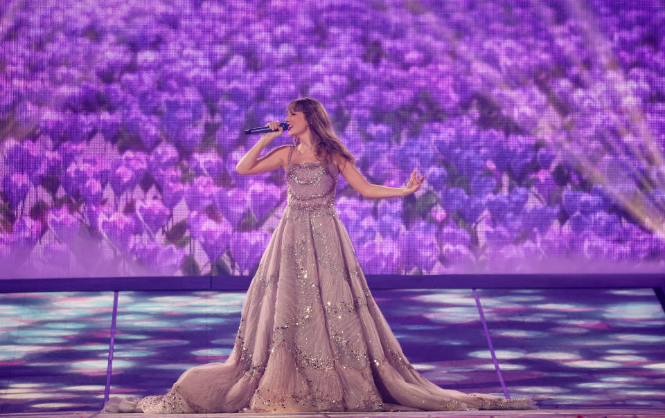 Taylor Swift, in a long mauve gown, sings onstage.